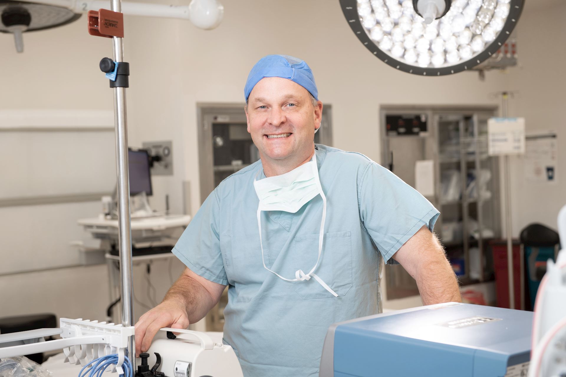 General surgeon smiling in operating room surrounded by medical equipment